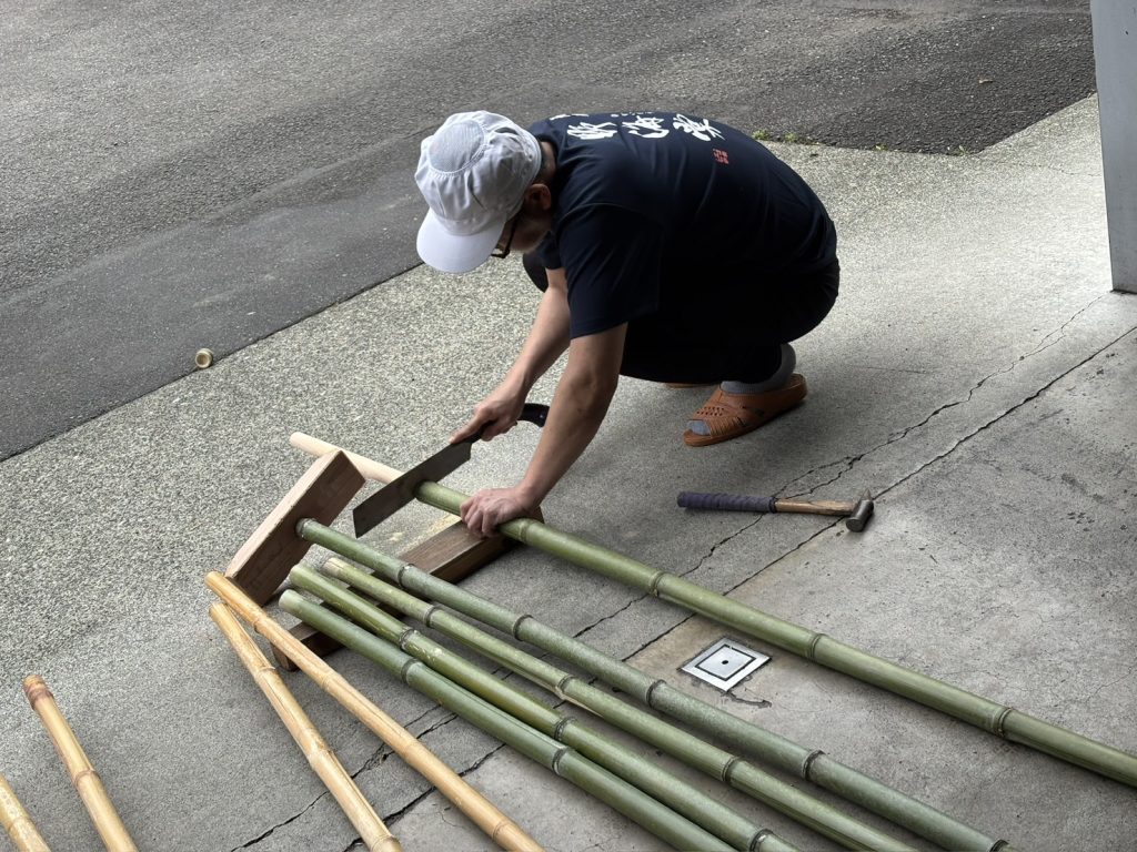 柄の先端に蕪の形をした台を取り付けるために、竹の空洞部分に木の棒を差し込んだ後、余分な部分をノコギリで切断している様子。